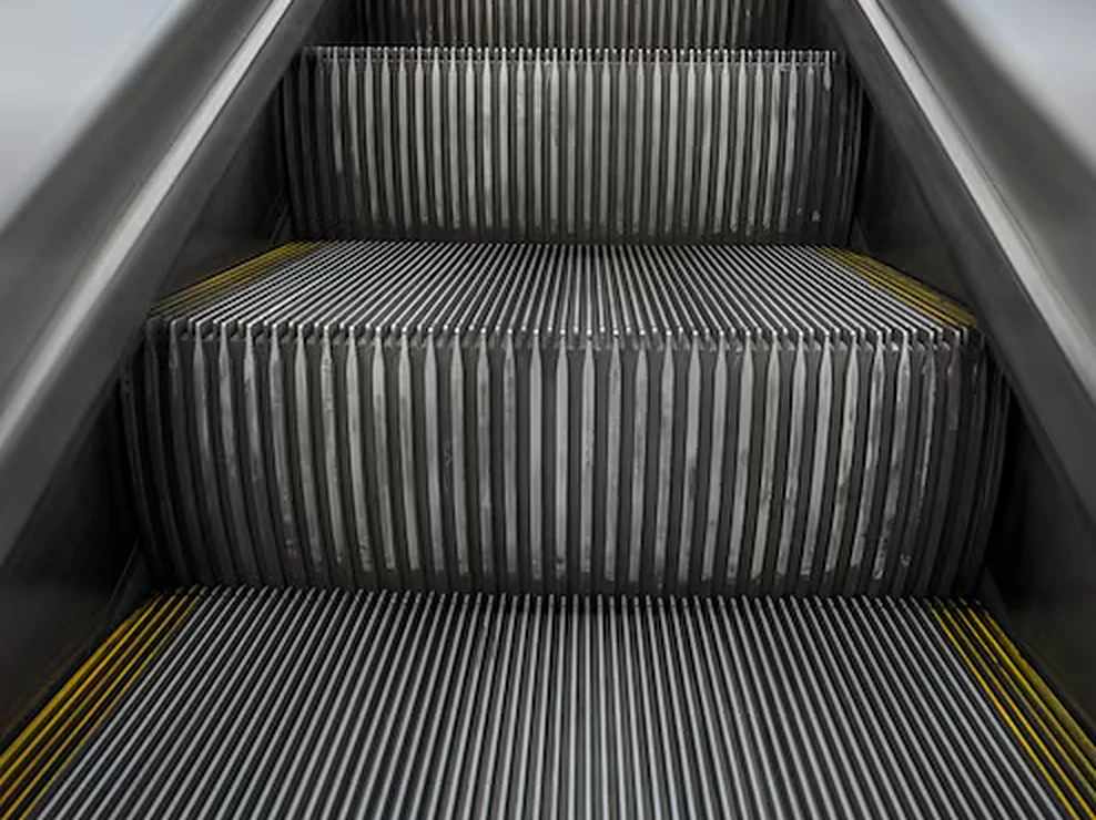 Close-up of escalator steps with grooved treads and yellow demarcation lines